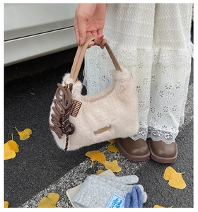 Detailed view of plush beige handbag featuring leather handles and cute baby charms