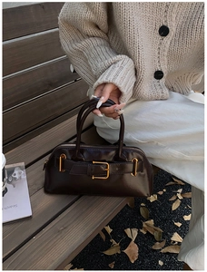 Detail of dark brown leather handbag with vintage gold buckle on a wooden bench