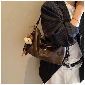 Detail der braunen Vintage-Schultertasche mit Plüschbär-Anhänger und Metallnieten