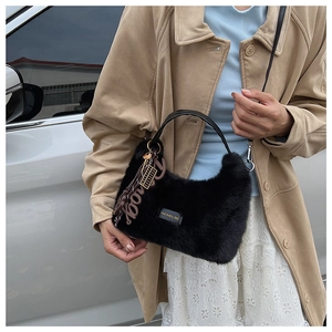 Detail shot of black faux fur plush handbag featuring leather tag and chic metal charm accessories