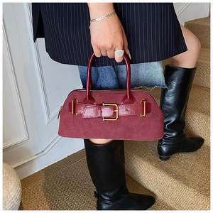 Detail of dark red suede handbag with gold buckle held by model in striped suit