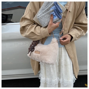 Detail of a beige faux fur shoulder bag with leather tag and decorative brown pendant charm