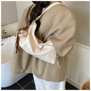 Detail der cremefarbenen Hobo-Tasche mit Bärenanhänger und khakifarbener Jacke
