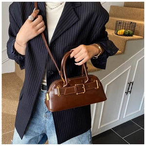 Detailed view of deep brown glossy leather handbag with vintage gold buckle on model