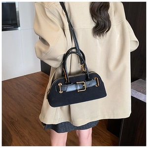Detail of black suede-textured shell bag with gold hardware worn with a beige blazer
