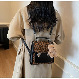Detail of trendy leopard print backpack featuring silver metal buckles and plush bear charm
