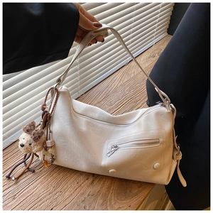Detailaufnahme der cremeweißen PU-Ledertasche mit Silberreißverschluss und Bärenanhänger