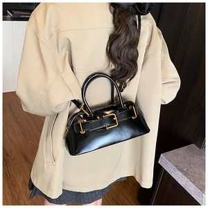 Detail of glossy black patent leather handbag with gold buckles on a beige blazer