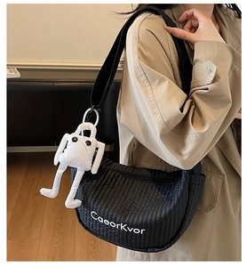 Detail of black quilted crescent bag with logo and cute plush charm on a shoulder strap