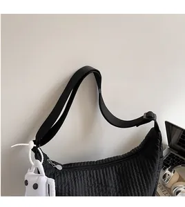 Close-up of black quilted dumpling bag with adjustable strap and cute plush charm