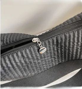 Detail of silver oval zipper on black quilted nylon bag with vertical wave pattern