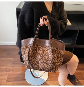 Close-up of leopard print tote bag featuring brown leather handles and metal rivet details