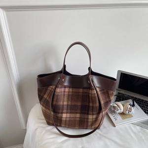 Detail of a brown leather and plaid tote bag with dual handles on a white desk