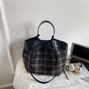 Close-up of checkered tote bag with leather trim alongside a laptop and headphones