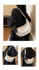Detailed view of white pleated dumpling bag featuring embroidered logo and monster charm