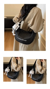 Detail of black quilted dumpling bag with a white plush doll charm and nylon strap