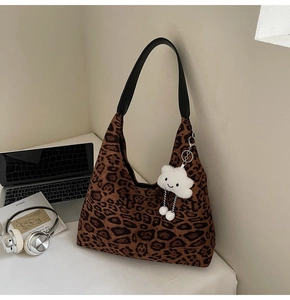 Hobo-Tasche mit Leopardenmuster, breitem Schultergurt und weißem Wolkenanhänger auf Tisch