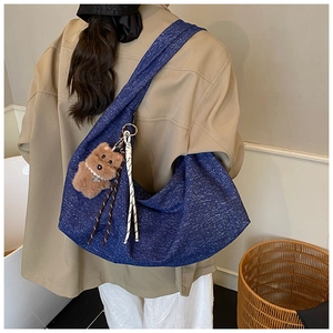 Detail of dark blue textured hobo bag with a brown plush bear pendant and knot detail