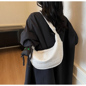 Detail of white quilted dumpling bag with adjustable strap and small black charm