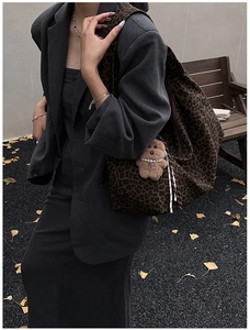 Close-up of leopard print tote bag with a small plush bear charm against autumn leaves