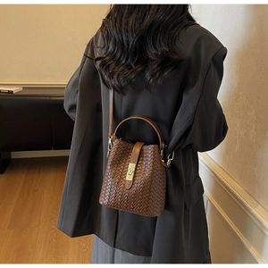 Detail of dark brown woven leather bucket bag with metal turn-lock and crossbody strap
