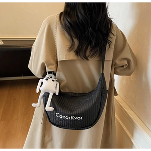Close-up of black quilted crescent bag with CaeorKvor text and white plush charm detail