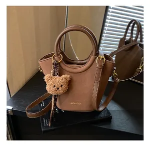 Détail du sac seau en daim marron foncé avec poignées en cuir et breloque ours