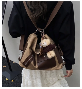 Rear view of model wearing a large brown canvas and leather backpack with a teddy bear charm