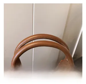 Gros plan de la poignée du sac en cuir marron avec coutures précises et anneau en métal