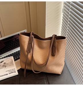 Detail shot of khaki woven tote bag showing embossed texture on a leather surface