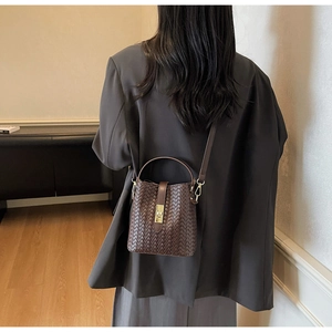 Detailed view of deep brown woven bucket bag with elegant golden clasp on a gray suit blazer