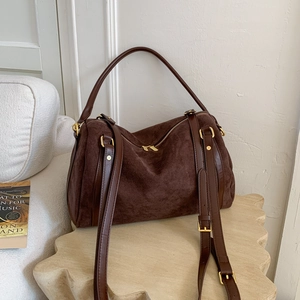 Détail du sac Boston en daim marron foncé avec finitions dorées sur socle en pierre