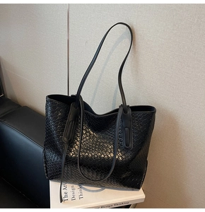 Close-up of black woven leather tote bag resting on design books in an elegant setting
