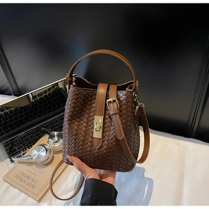 Detail of dark brown woven leather bucket bag featuring a gold lock and cross body strap