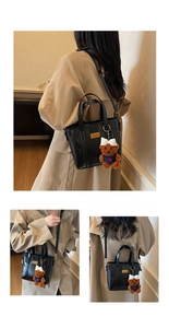 Detail of black crossbody bucket bag with cute brown teddy bear charm and gold hardware