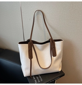 Detailed view of cream woven tote bag with brown straps on a black book prop