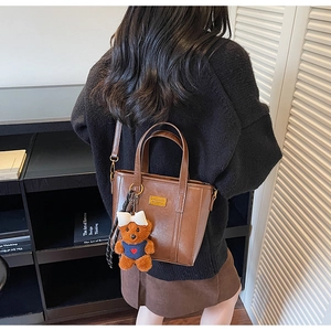 Detail view of brown PU leather tote bag with teddy bear charm and silk scarf