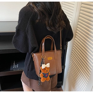 Detail of dark brown faux leather tote bag with dual handles and cute teddy bear charm