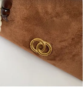 Detail of caramel suede handbag showing golden double ring hardware and decorative wood beads