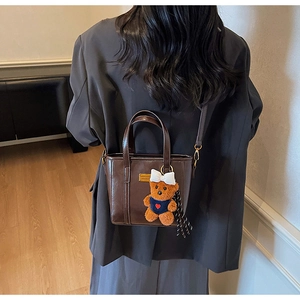 Detail of dark brown leather tote bag with gold plaque and plush bear charm on model