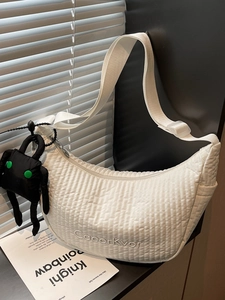 White quilted croissant bag with plush pendant and embroidered logo on wide strap