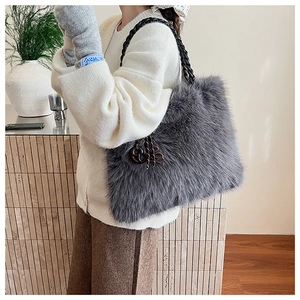 Detail of plush grey faux fur tote bag with black chain strap and metal charm on a model