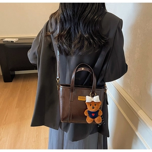 Polished brown tote bag with bear charm shown in a stylish crossbody and handbag view