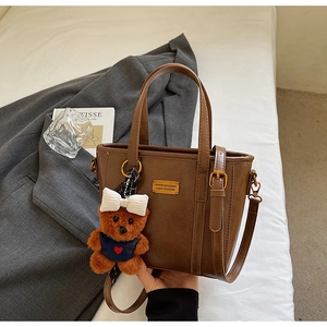 Detail of dark brown leather tote featuring gold metal nameplate and plush bear charm