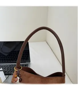 Detail of soft brown suede shoulder bag featuring leather handle and colorful beaded charm