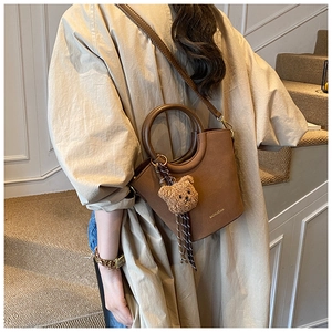 Sac seau marron avec charme d'ours en peluche porté par un mannequin dans un intérieur