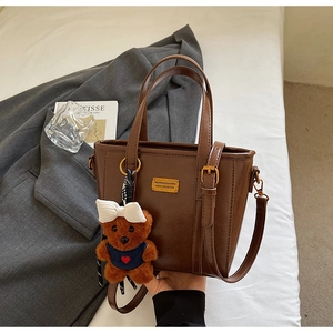 Close-up of brown matte tote bag with gold logo plaque and cute teddy bear pendant