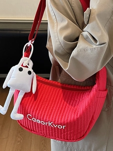 Red quilted dumpling crossbody bag with cute white charm worn by model in trench coat