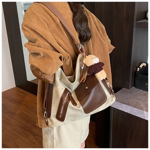 Detail of canvas tote bag showing brown leather pockets, wide strap and cute bear charm