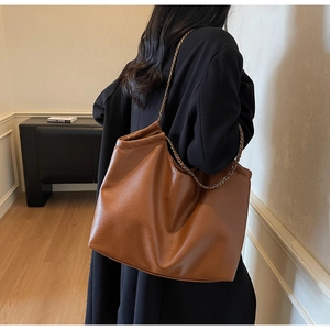 Detail of a brown leather tote bag showing a leather-metal chain strap and embossed logo